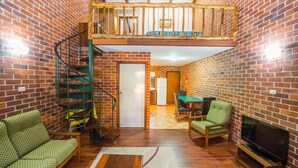 A loft-style room with exposed brick walls, a wooden staircase, a dining area, and a television. - Evedon Park Bush Retreat (Burekup)