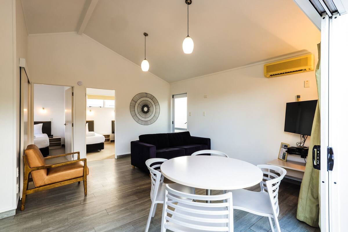 Una sala moderna con una mesa de comedor redonda, sillas blancas, un sofá oscuro y un banco de madera.