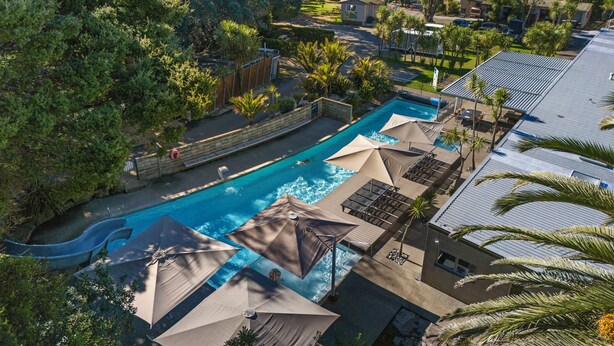 Zona de piscina con sombrillas y sillas reclinables, rodeada de árboles y vistas al océano.