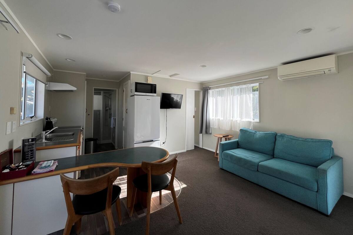 Un espacio habitable compacto con kitchenette, comedor, sofá y televisor montado en la pared.