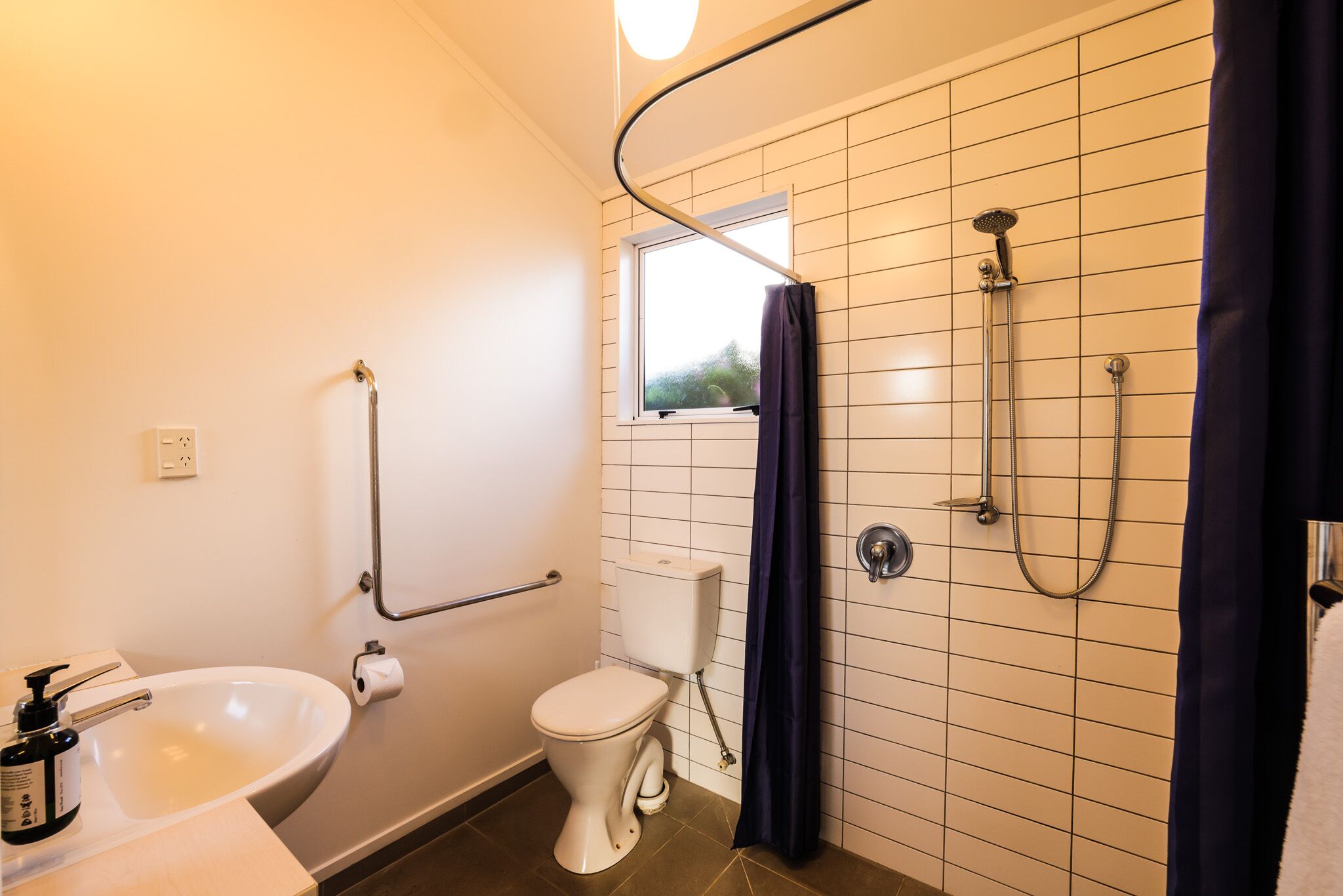 A bathroom with a white sink, a toilet, a window, and a shower with a curtain.
