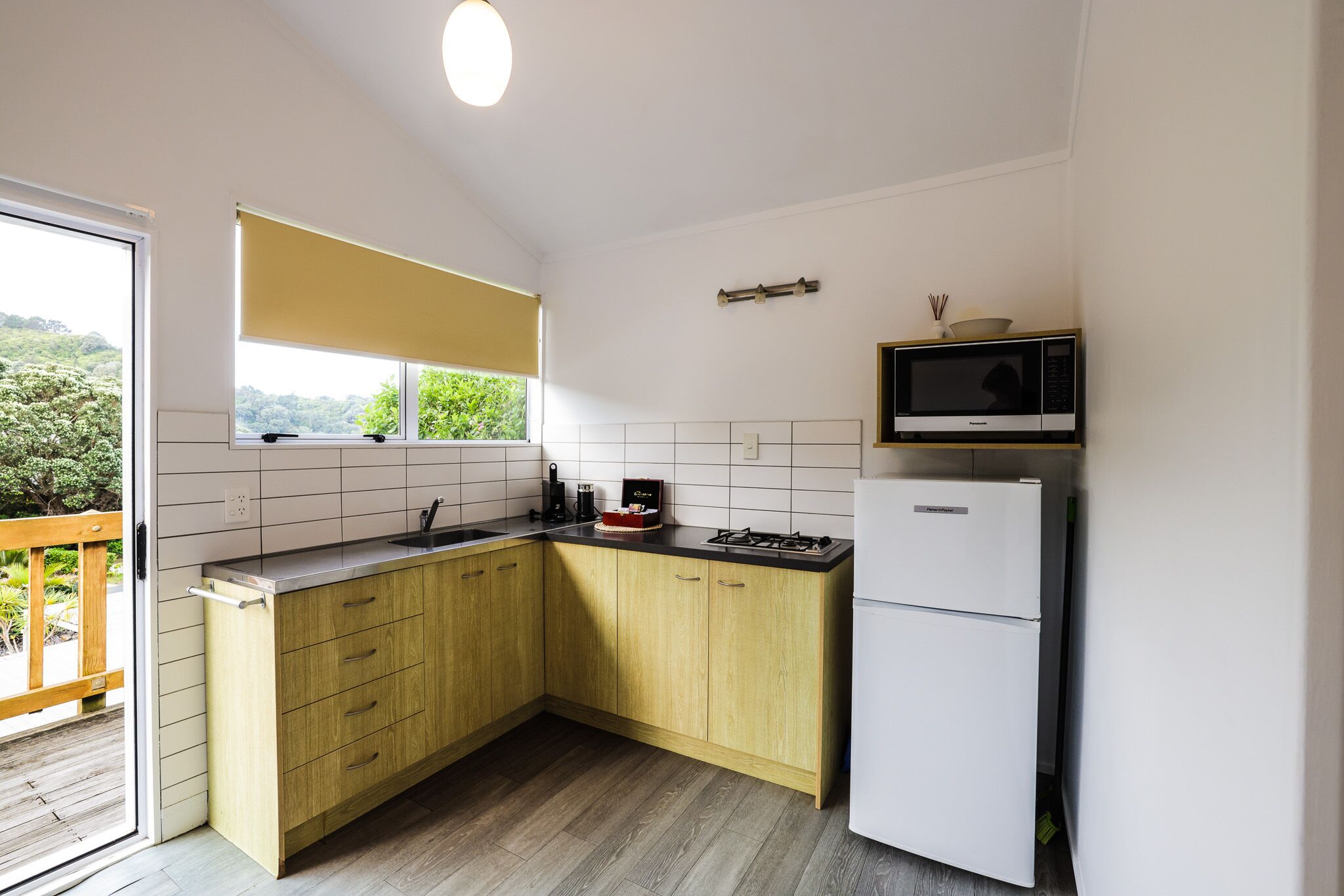 A kitchen with wooden cabinets, a white refrigerator, a microwave, and a window with a view of greenery.
