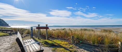 A bench at a beach entrance with a sign indicating beach access.
