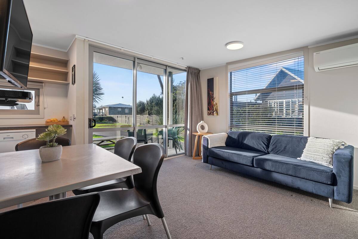 Una sala de estar moderna con comedor, ventanas amplias, un sofá y un televisor.
