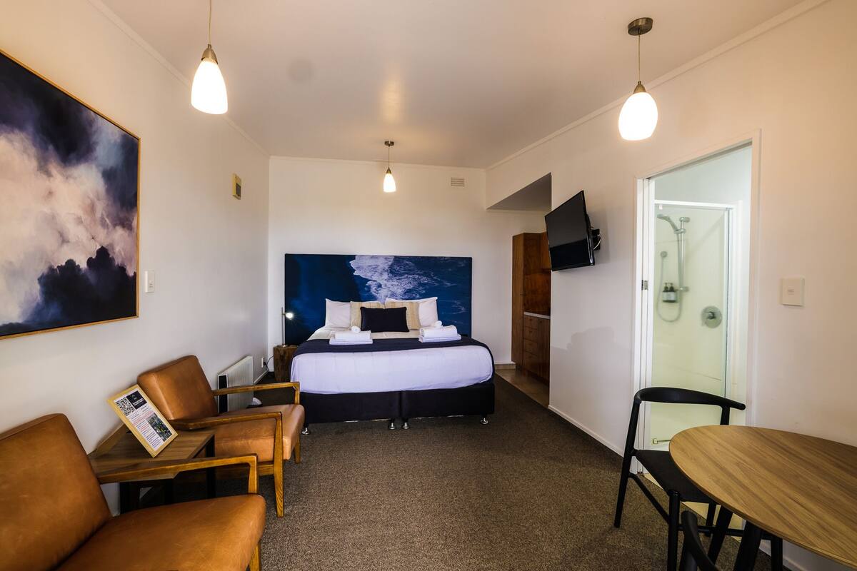 Habitación de hotel con cama, escritorio, silla, mesa, televisor y ducha.