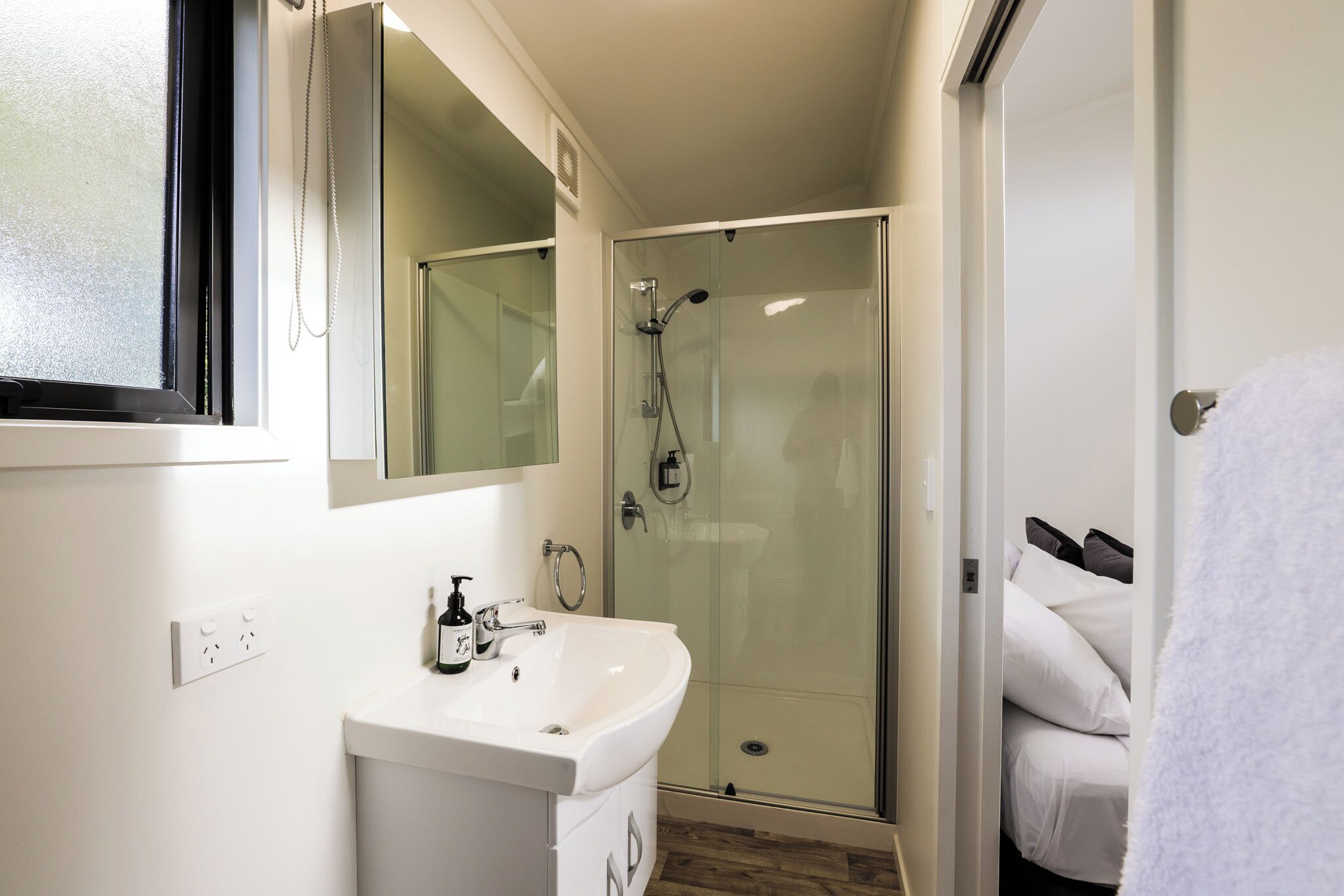 Un baño moderno con ducha de vidrio, lavamanos blanco y espejo encima.