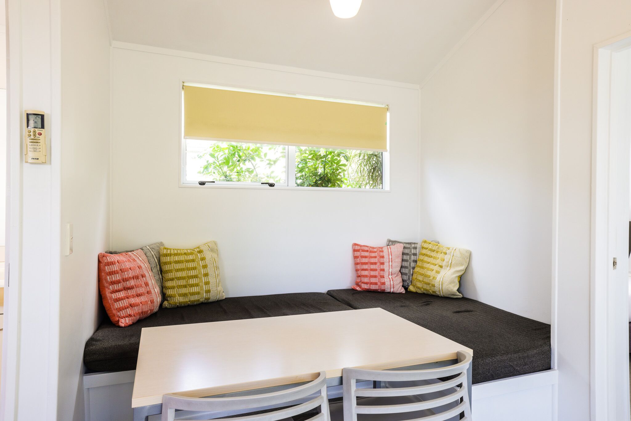 Um quarto acolhedor com um banco e mesa embutidos, uma janela com persiana amarela e um termostato na parede.