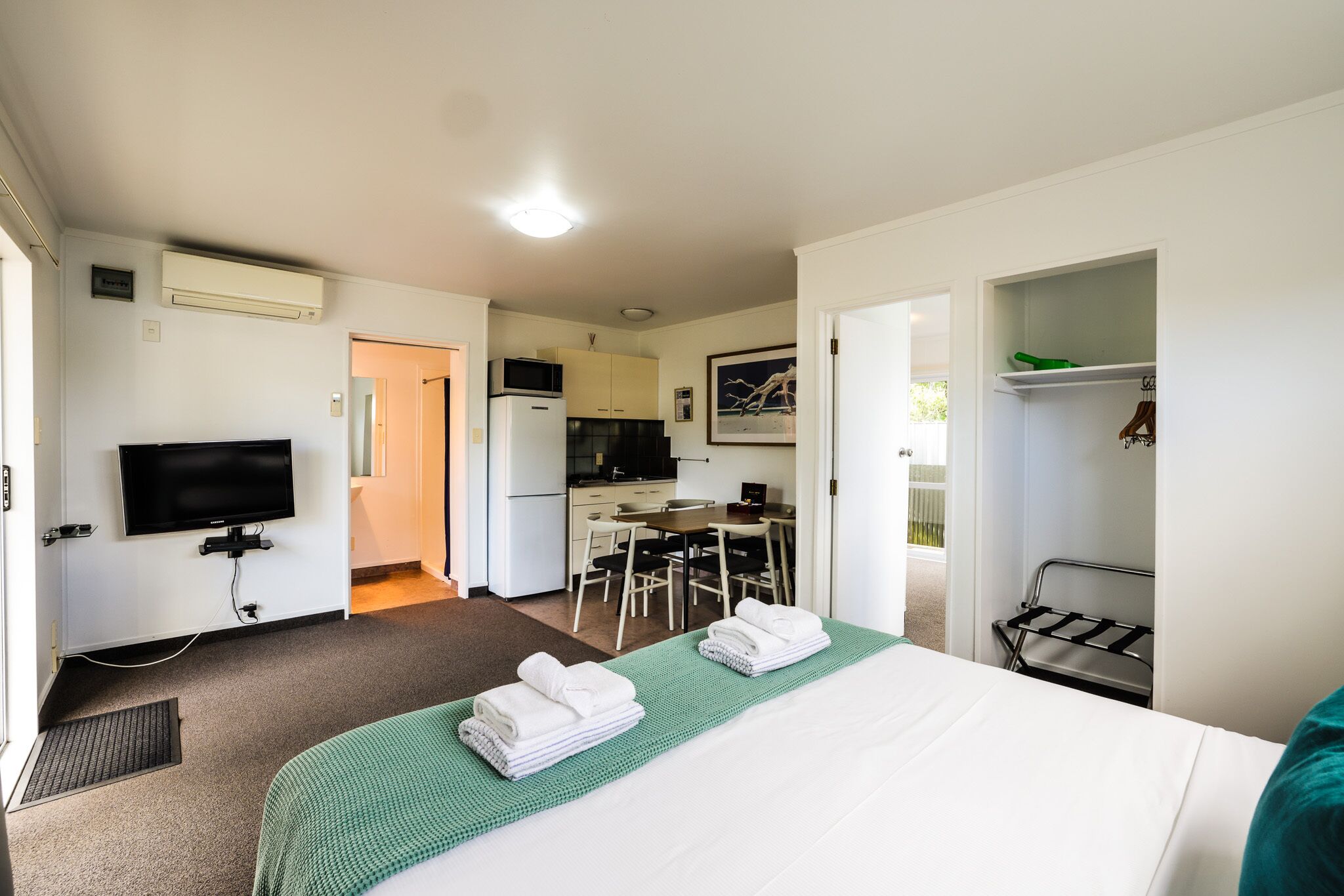 Una habitación de hotel con una cama, televisor, kitchenette y zona de comedor.
