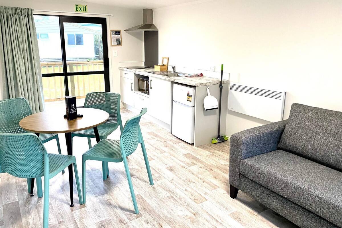 Una habitación compacta con una mesa de comedor y sillas, una kitchenette, un sofá y vistas a través de una ventana.