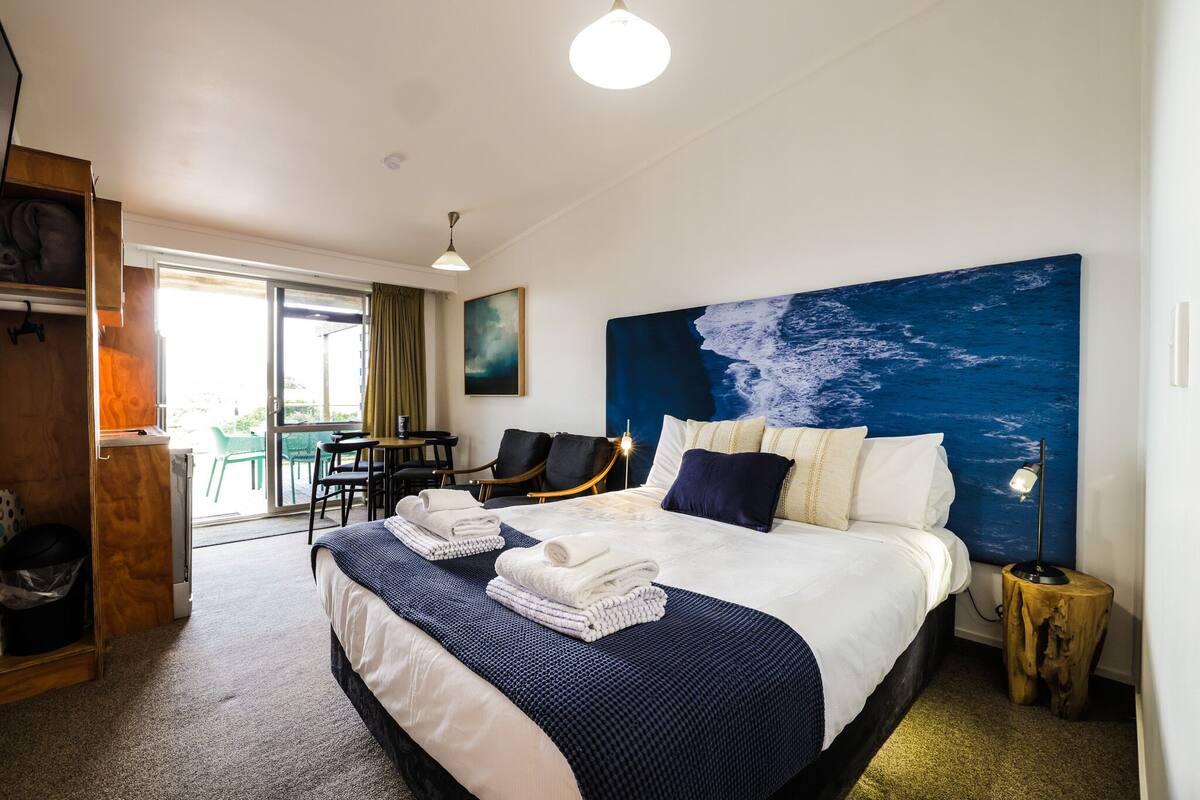Habitación de hotel con una cama grande, vistas al exterior, zona de comedor y un aparador de madera.