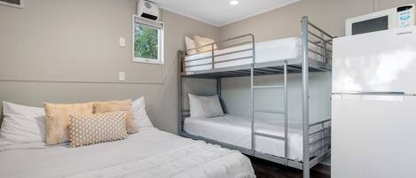 Habitación con literas, una refrigeradora blanca y una ventana con vista a árboles.
