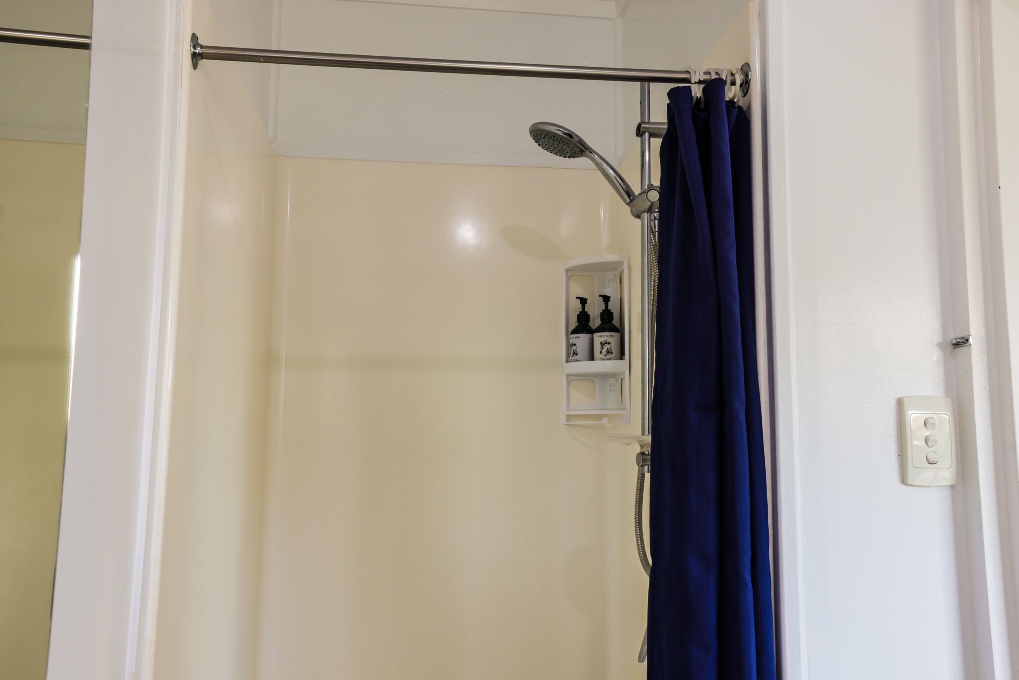 A shower area with a handheld showerhead, a towel rack, and a shelf with toiletries.
