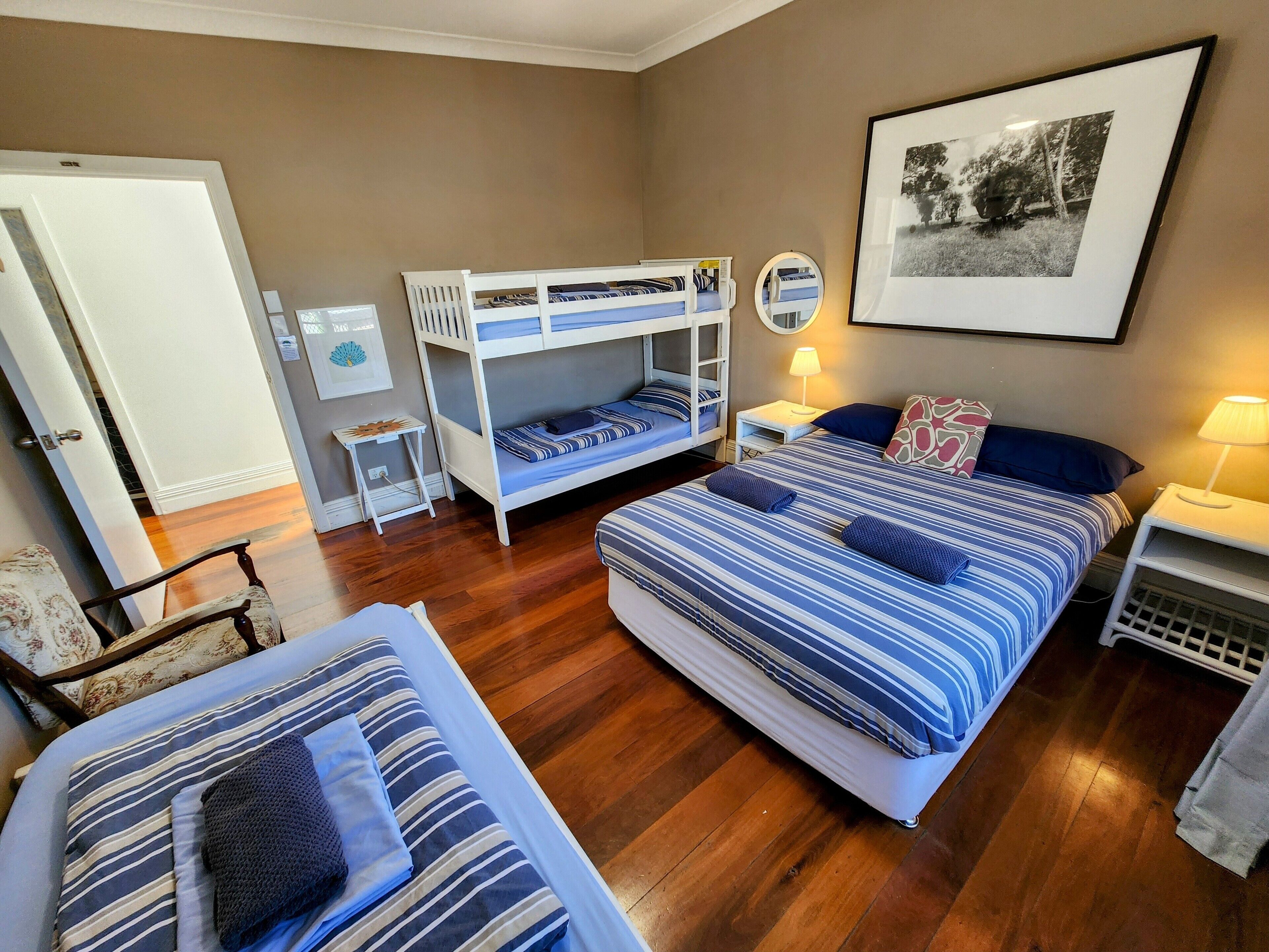 Un dormitorio con dos camas, una litera, suelo de madera, un cuadro en la pared y una mesita de noche con una lámpara.