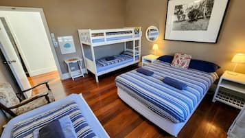 Un dormitorio con dos camas, una litera, suelo de madera, un cuadro en la pared y una mesita de noche con una lámpara.
