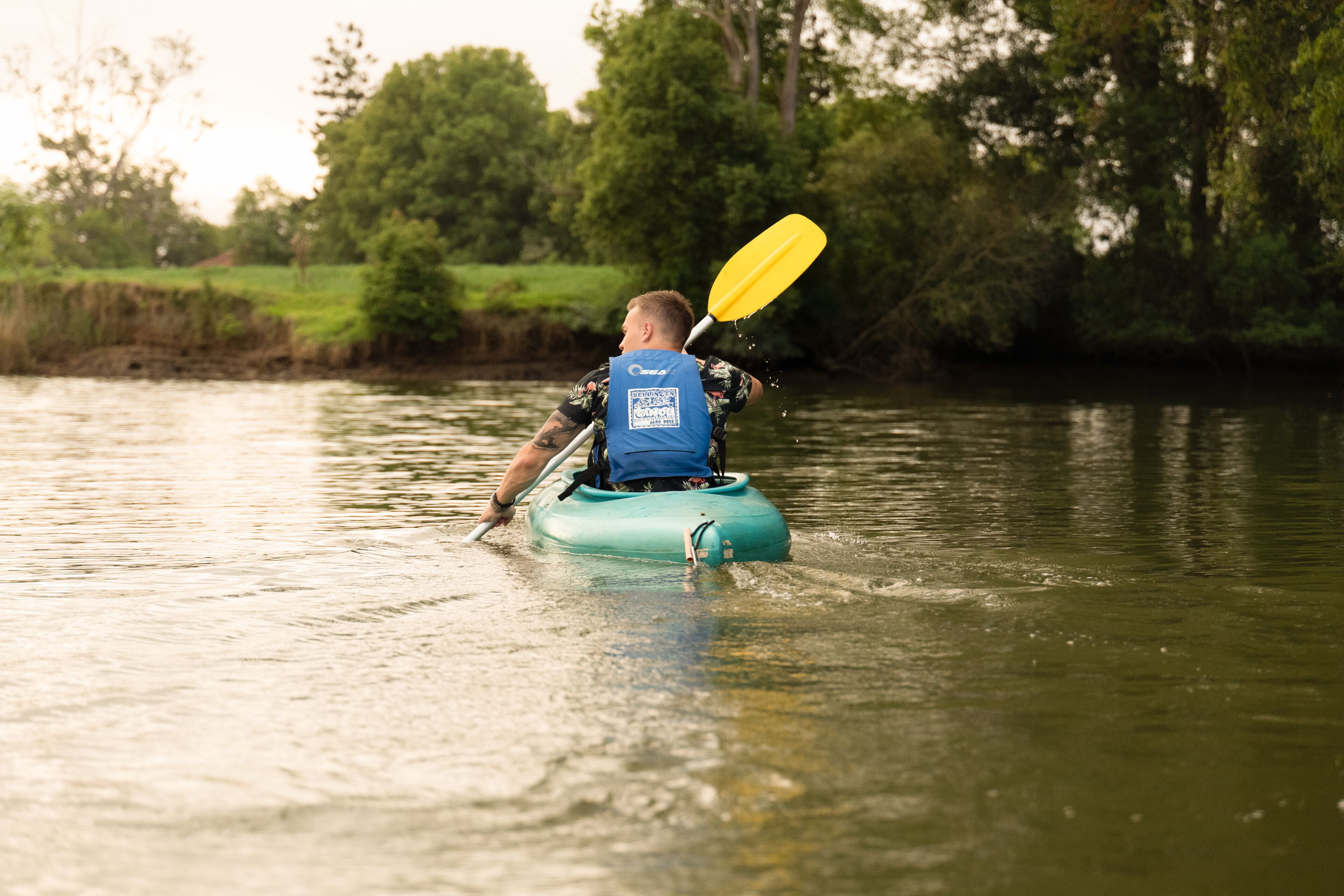 Una persona practica kayak en un río tranquilo bordeado de vegetación.