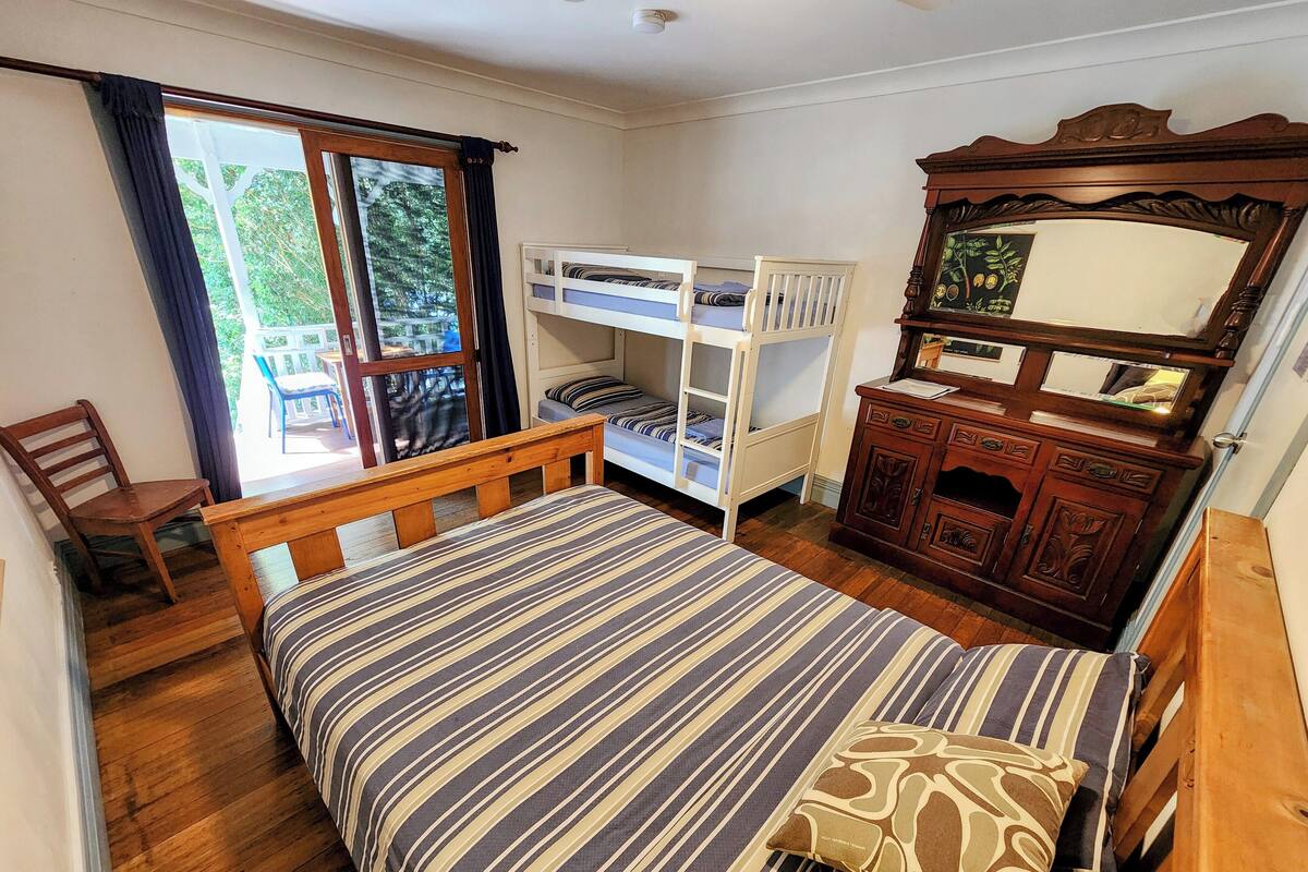 Ein Schlafzimmer mit einem Bett, einem Holzstuhl, einer Kommode mit Spiegel und einem Fenster mit Vorhängen.