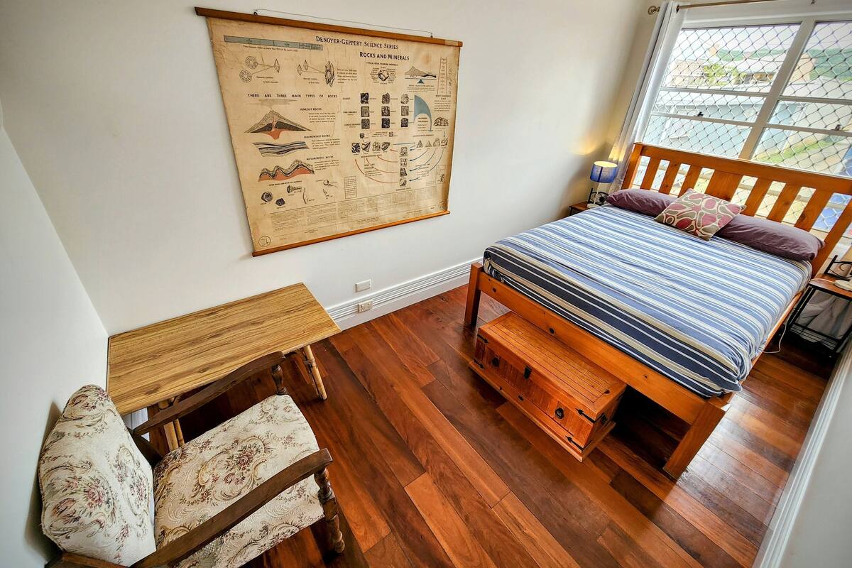 Ein Schlafzimmer mit einem Bett, einem Holztisch, einem Stuhl und einem Bild an der Wand.