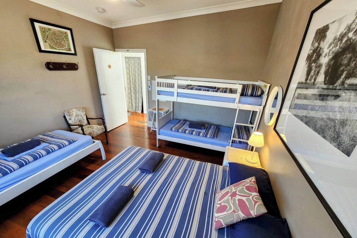 Ein Zimmer mit zwei Einzelbetten, einem Etagenbett, einem Sessel und einem gerahmten Bild an der Wand.