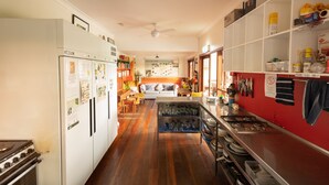 A kitchen with a refrigerator, stove, and cabinets. There is a dining area with a table and chairs. - The Belfry Guesthouse (Bellingen)