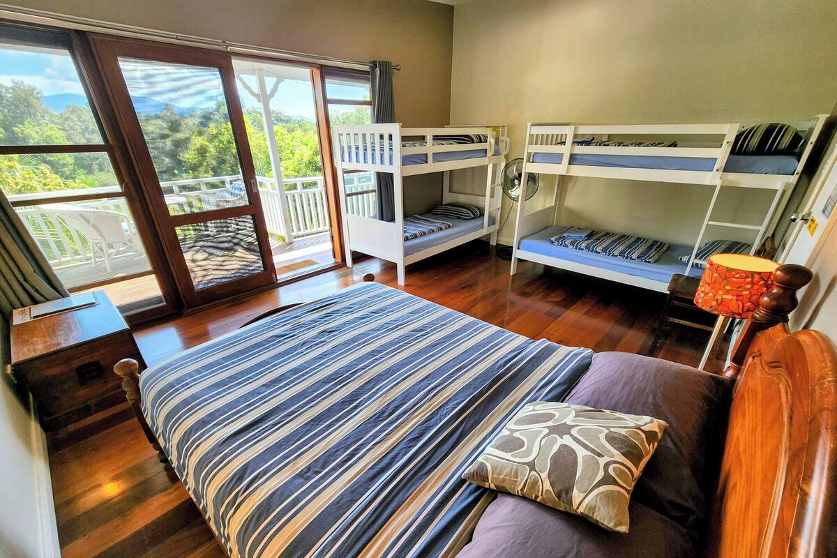 Ein Zimmer mit einem großen Bett, zwei Etagenbetten, Holzboden und Blick durch eine Glastür.