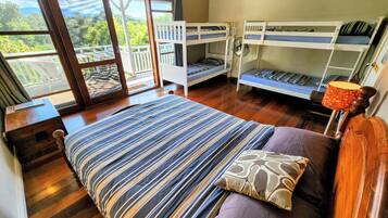 A room with a large bed, two bunk beds, a wooden floor, and a view through a glass door.