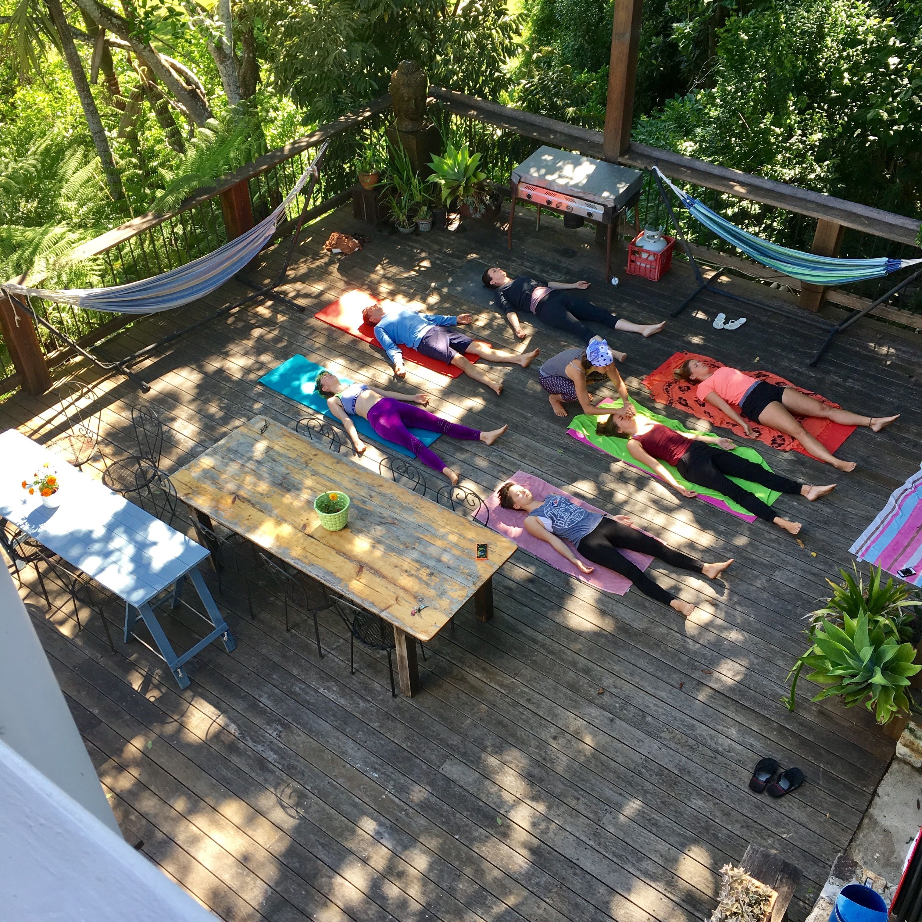 Un gruppo di persone su tappetini da yoga all'aperto, su un molo di legno circondato dal verde.