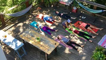 Un gruppo di persone su tappetini da yoga all'aperto, su un molo di legno circondato dal verde.