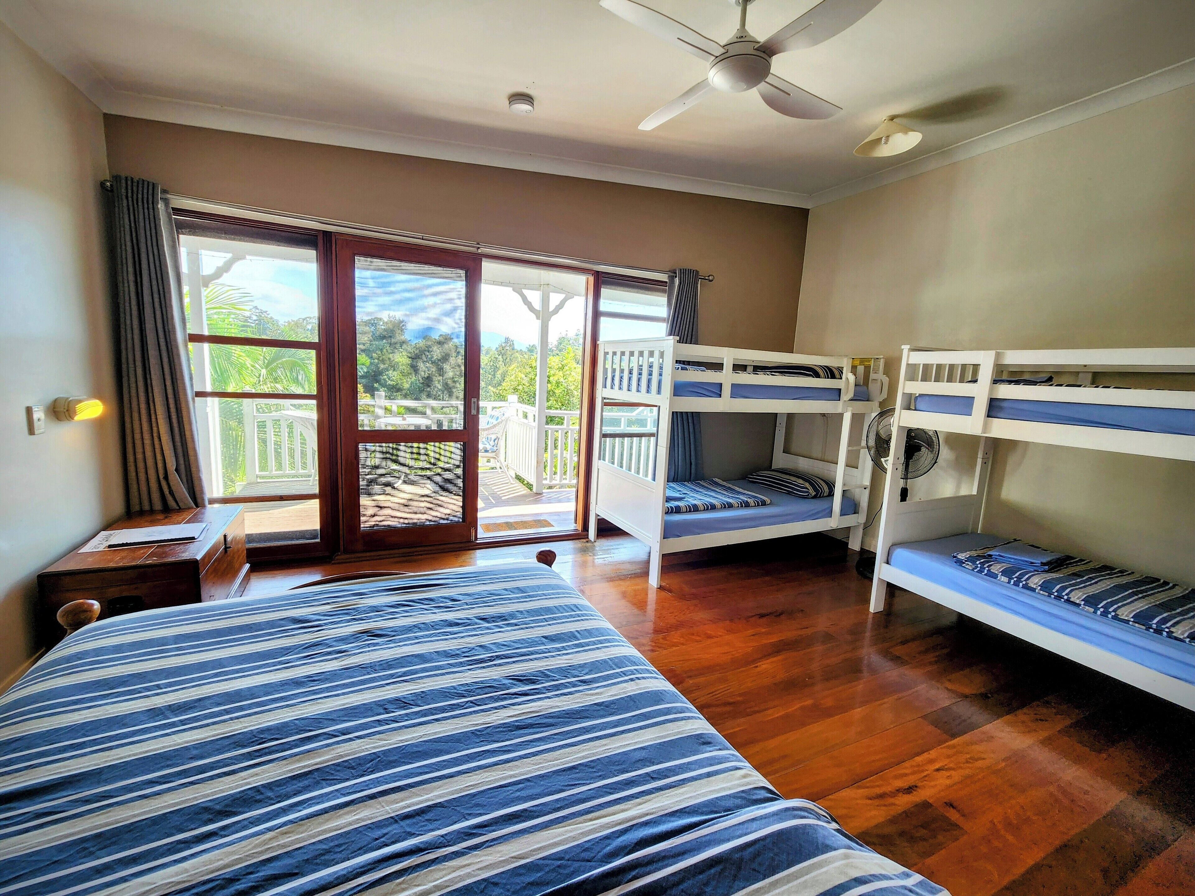 A room with a bunk bed, a desk, and a balcony with a view of greenery.