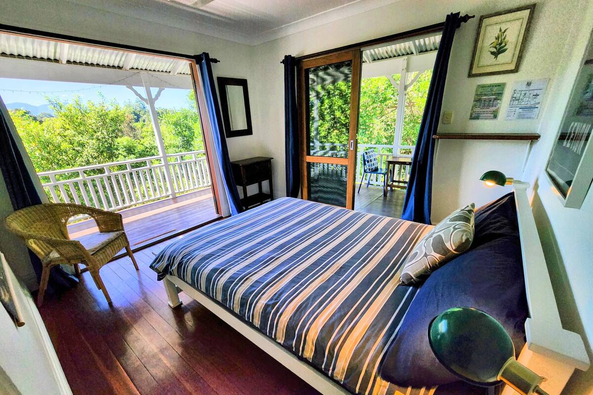 Ein Schlafzimmer mit Bett, Sessel, Schreibtisch und einem Balkon mit Blick auf Grünfläche.