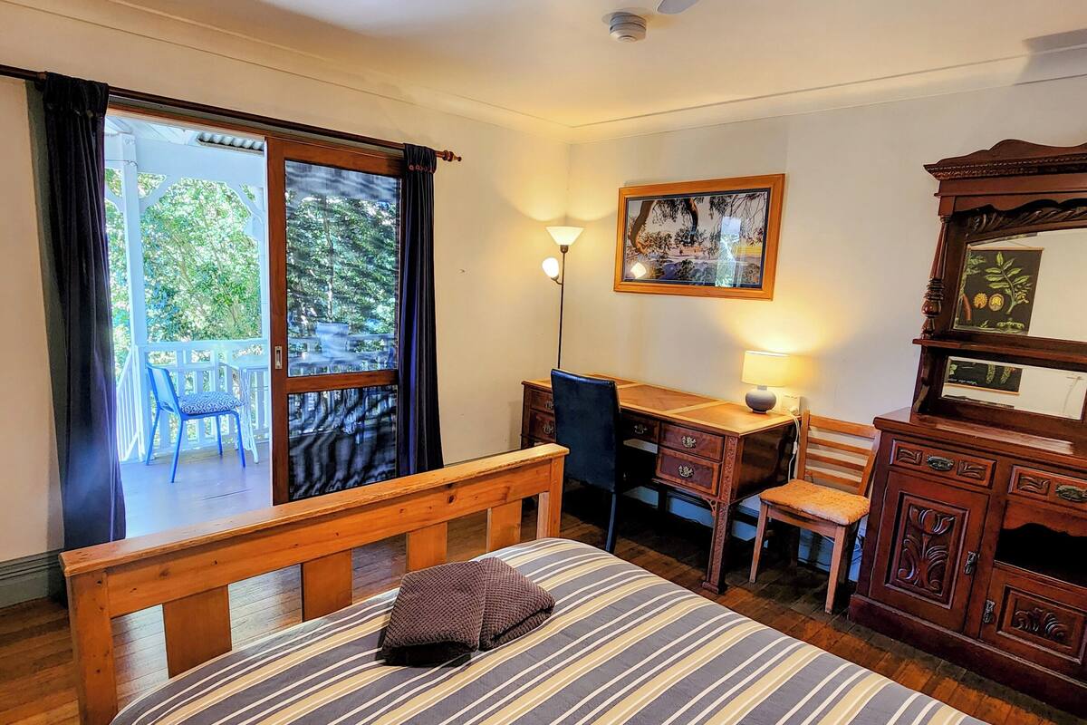 Ein Zimmer mit einem Bett, einem Schreibtisch, einem Stuhl, einer Kommode und einem Fenster mit Vorhängen.