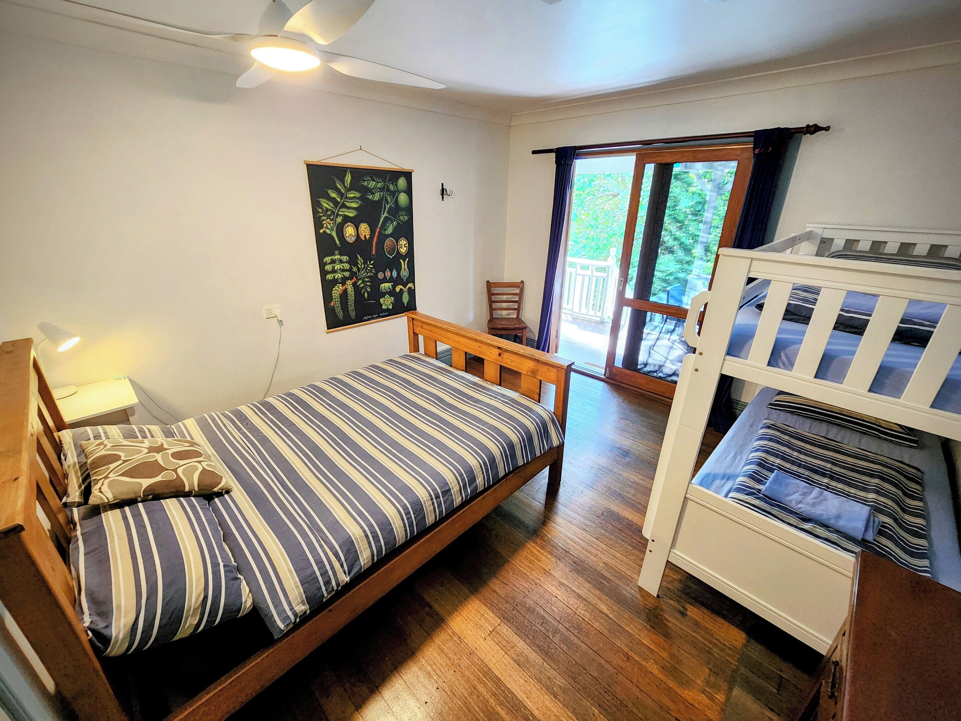 A bedroom with a single bed, a wooden bench, a small table, and a window with a view of greenery.