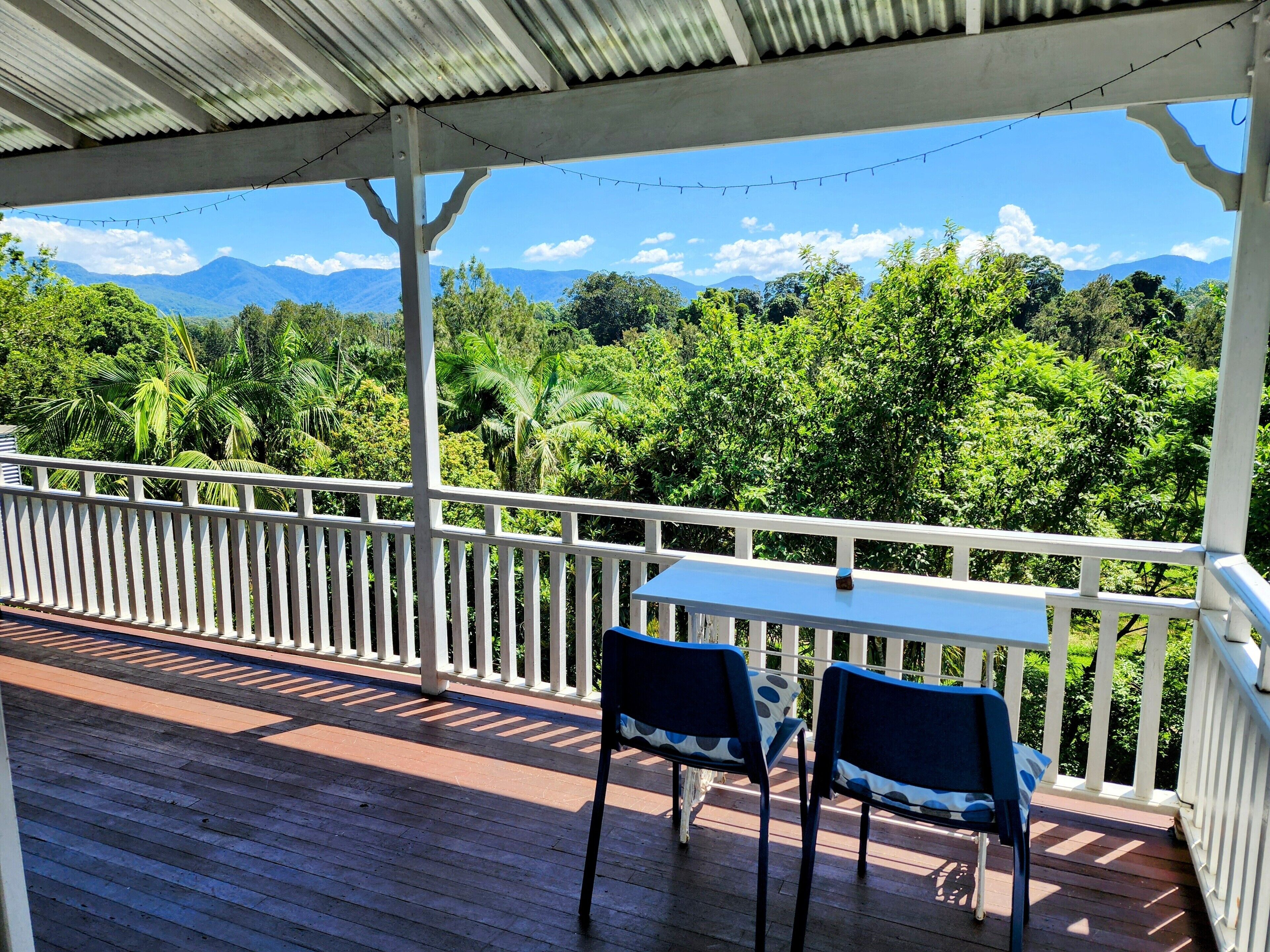 A covered outdoor area with a table and chairs, overlooking a lush green landscape with mountains in the distance.
