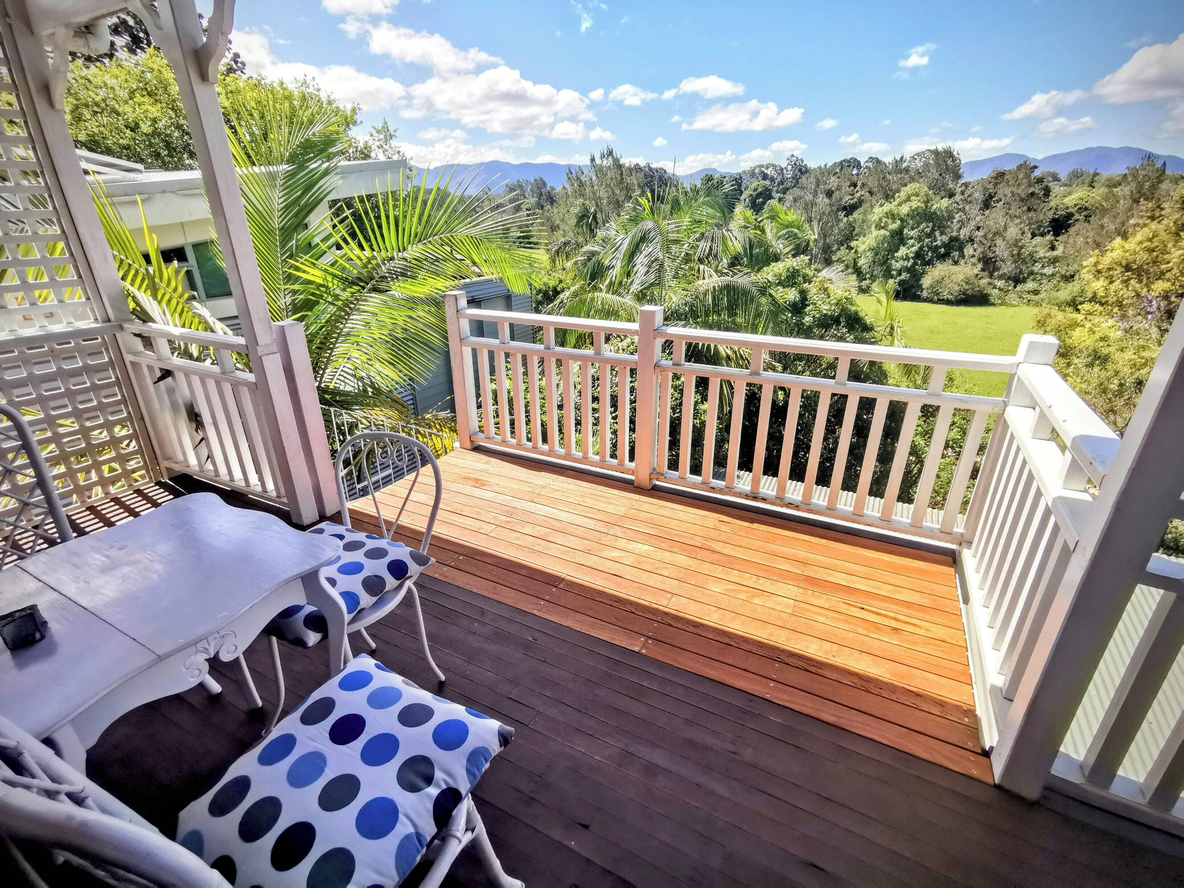 A wooden deck with a white railing, a table with a polka dot cushion, and a chair.
