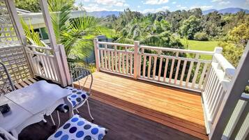 A wooden deck with a white railing, a table with a polka dot cushion, and a chair.