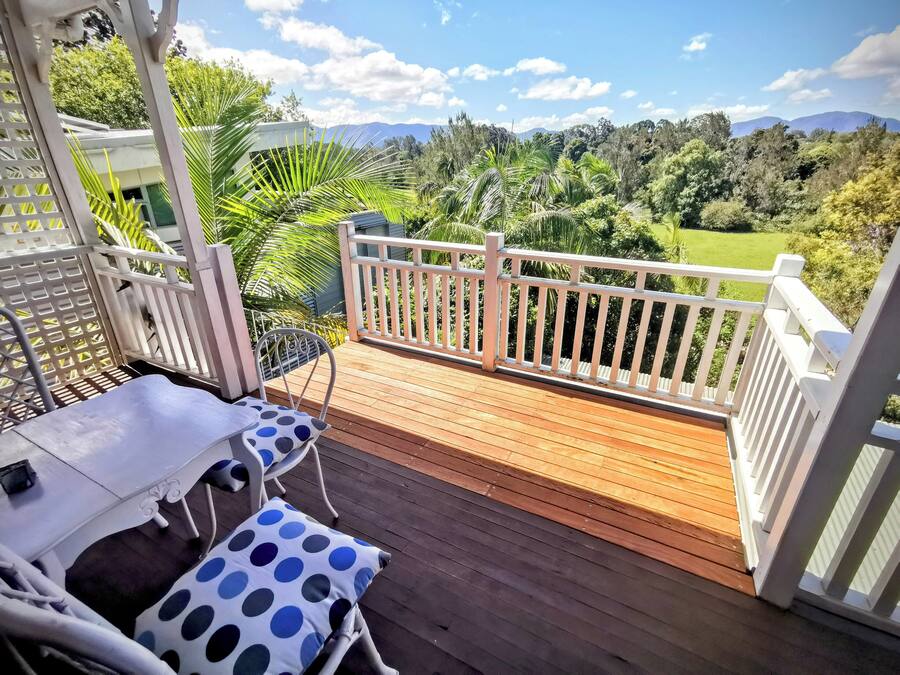 Una terraza de madera con barandilla blanca, una mesa con cojín de lunares y una silla.