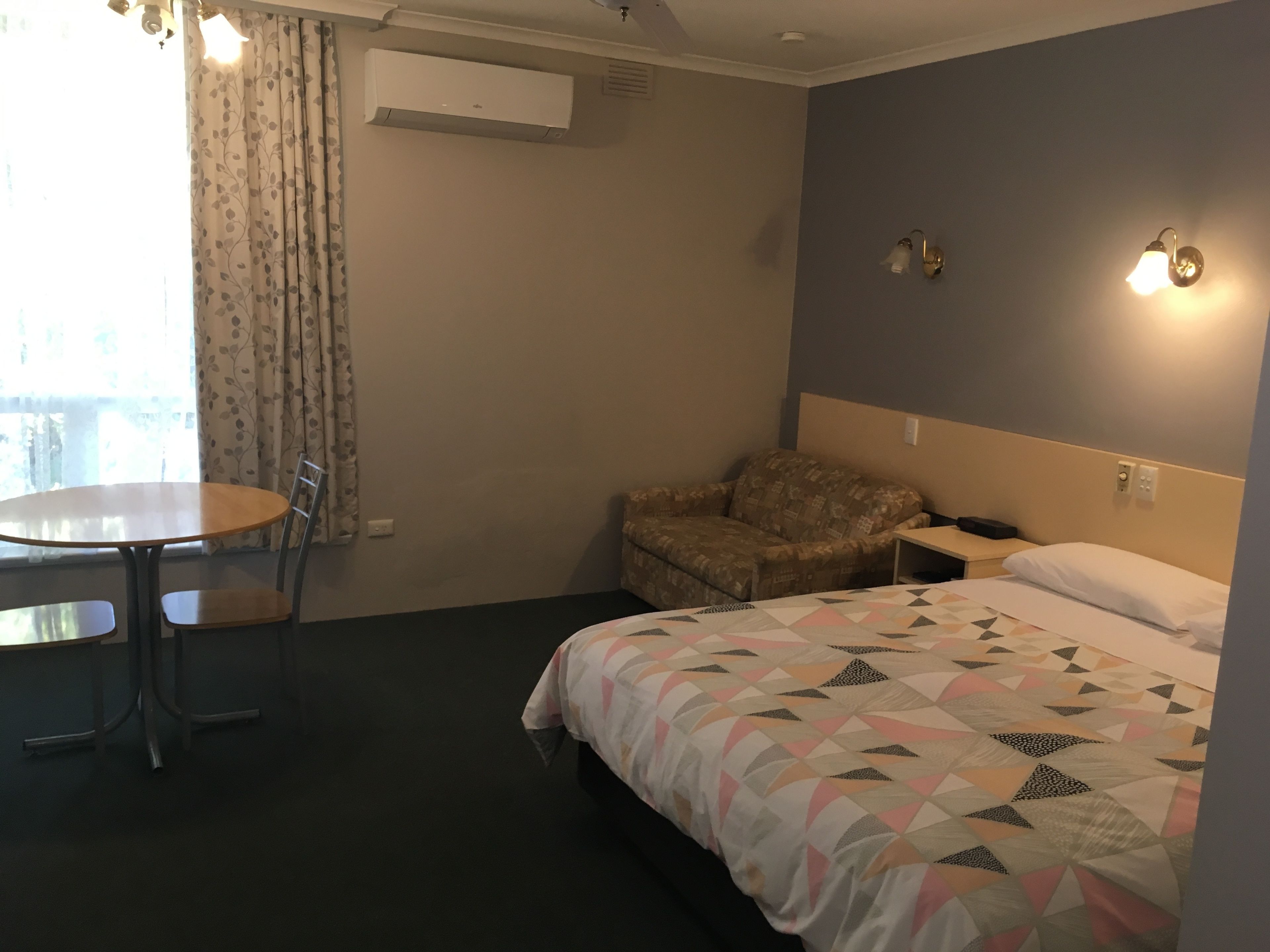 A hotel room with a bed, a chair, a table, and a window with curtains.