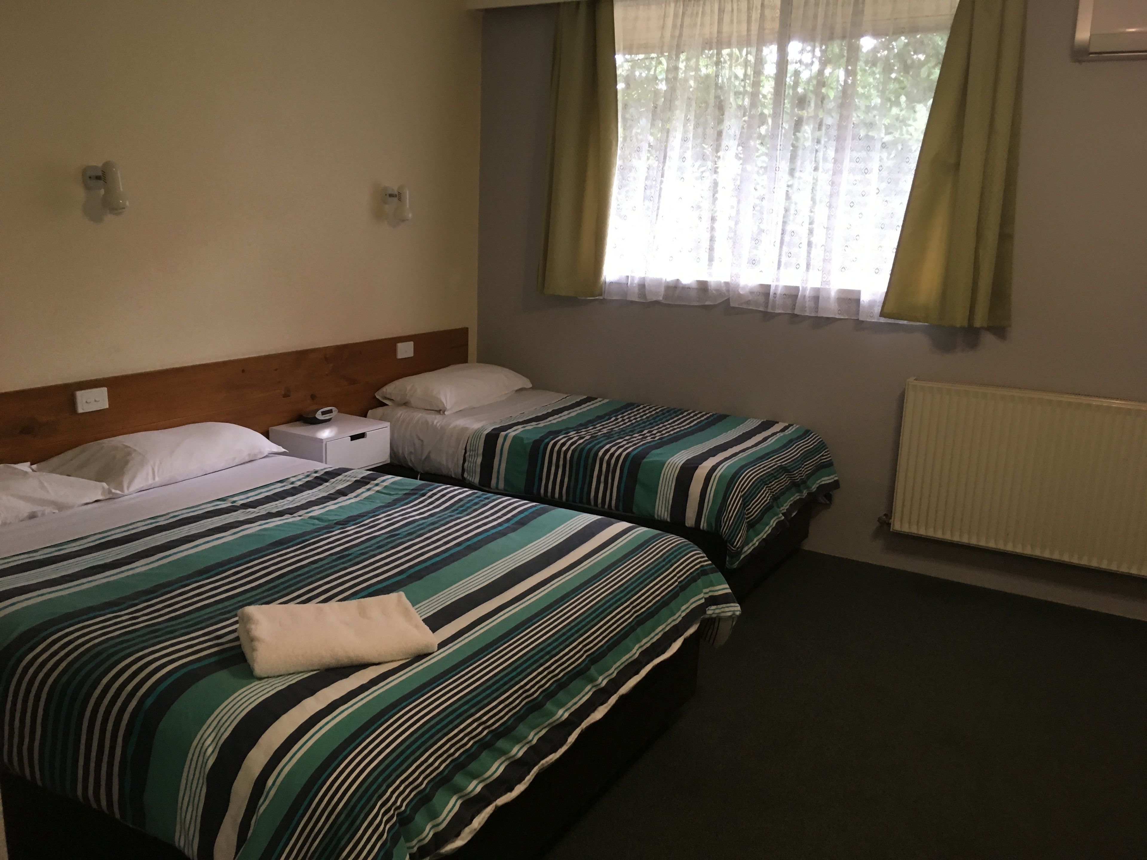 Habitación de hotel con dos camas, cada una con ropa de cama a rayas, una mesita de noche con un reloj y una ventana con cortinas.