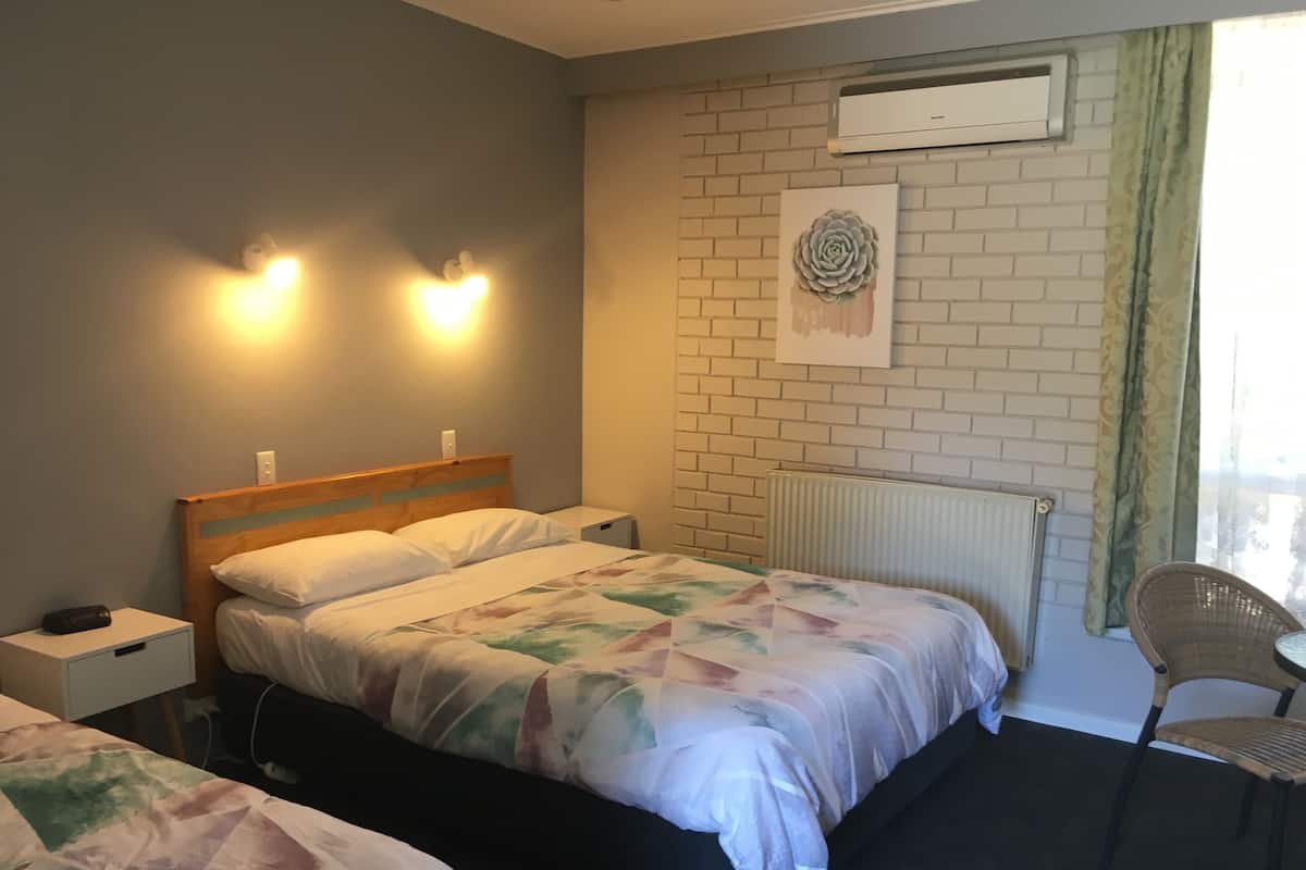 A hotel room with a bed, bedside table, lamp, and a chair.