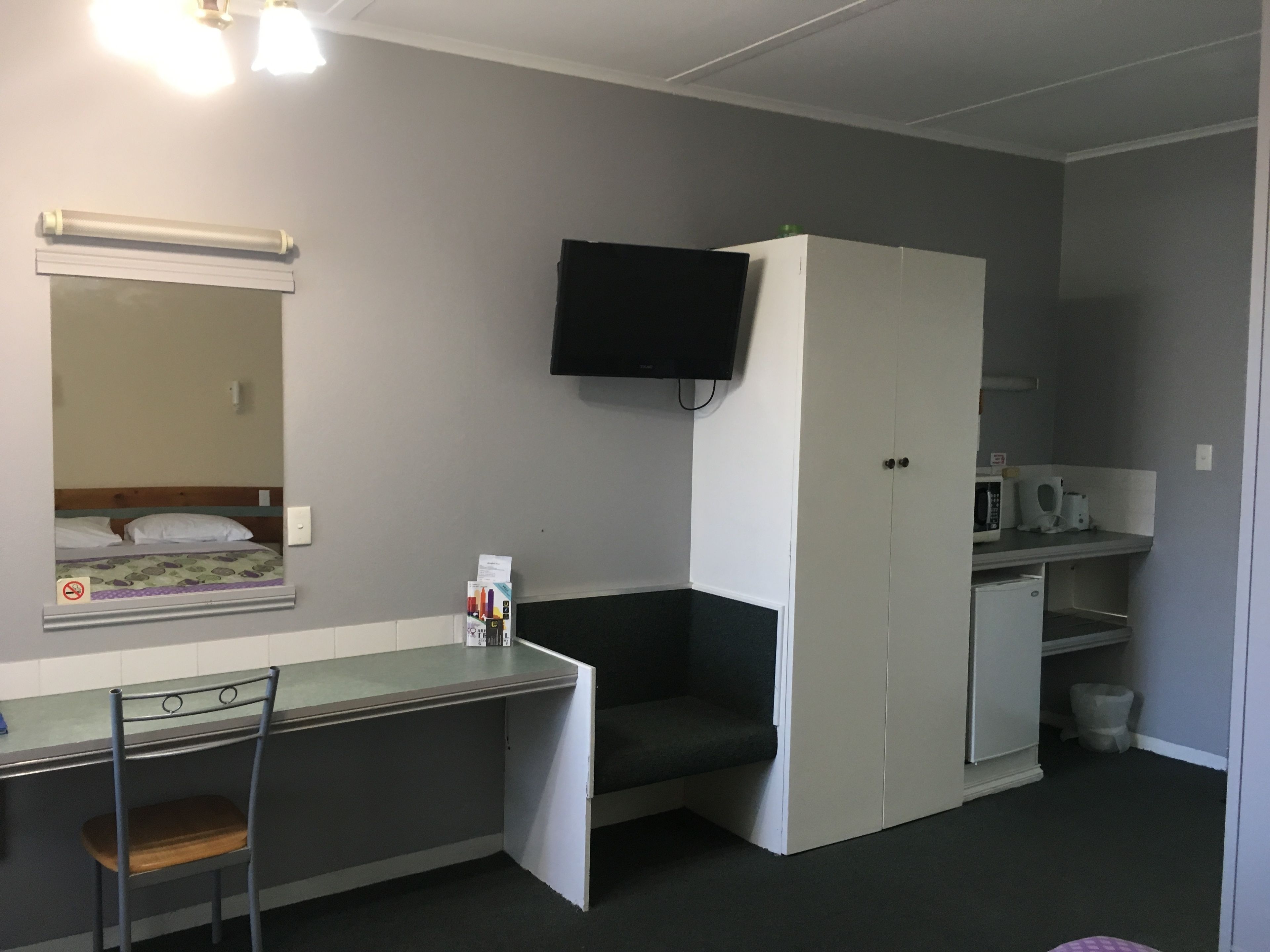 Ein kleines Zimmer mit einem Bett, einem Schreibtisch, einem Stuhl, einem Fernseher und einer Mikrowelle.