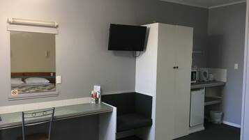 Ein kleines Zimmer mit einem Bett, einem Schreibtisch, einem Stuhl, einem Fernseher und einer Mikrowelle.