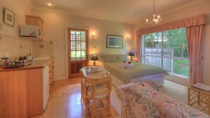 A cozy bedroom with a bed, a bedside table, a chair, a window with curtains, a lamp, and a view of greenery outside. - Chalets Lumineux (Bright)