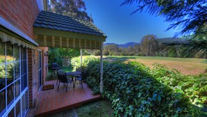 A patio with a table and chairs, a brick wall, and a view of a grassy field and trees. - Chalets Lumineux (Bright)