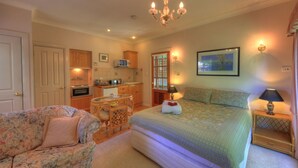 A cozy bedroom with a bed, a chair, a small table, and a kitchenette. - Chalets Lumineux (Bright)