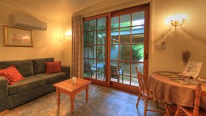 A cozy living room with a sofa, a coffee table, and a dining table with chairs. There is a large window with curtains, and a wall-mounted air conditioner. - Chalets Lumineux (Bright)