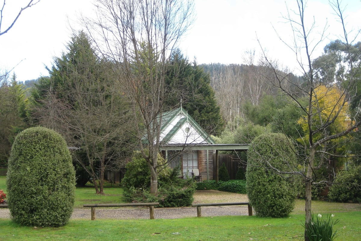 A small building with a green roof, surrounded by well-maintained hedges and trees.