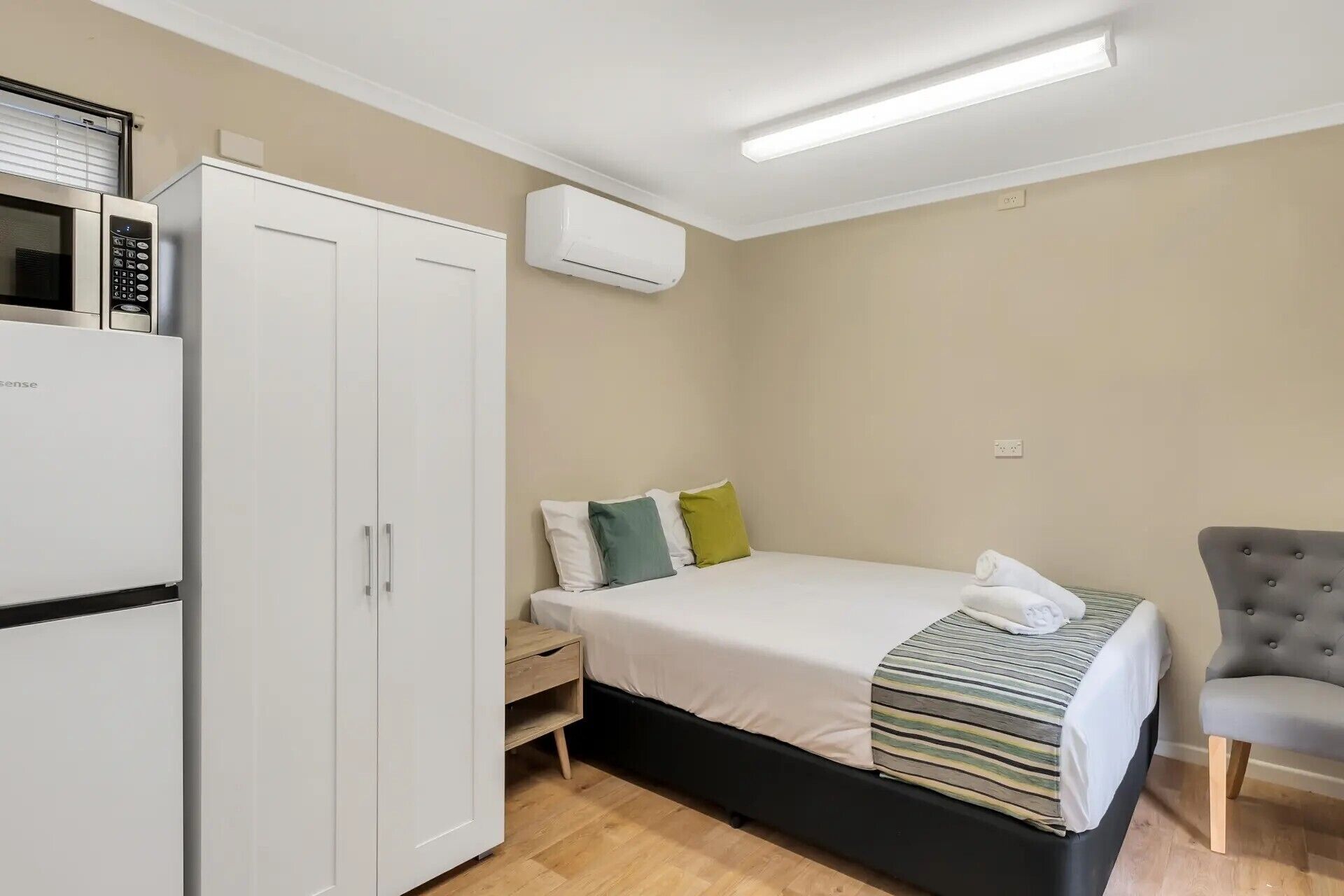 Een kleine hotelkamer met een bed, een kledingkast, een bureau en een stoel.