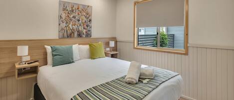 A neatly arranged hotel room with a large bed, a bedside table with a lamp, a wall-mounted mirror, and a painting above the bed.