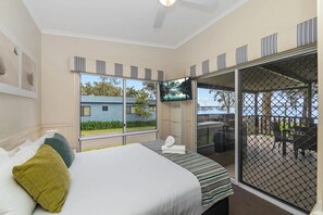Een slaapkamer met een bed, een televisie en uitzicht op een huis en water.