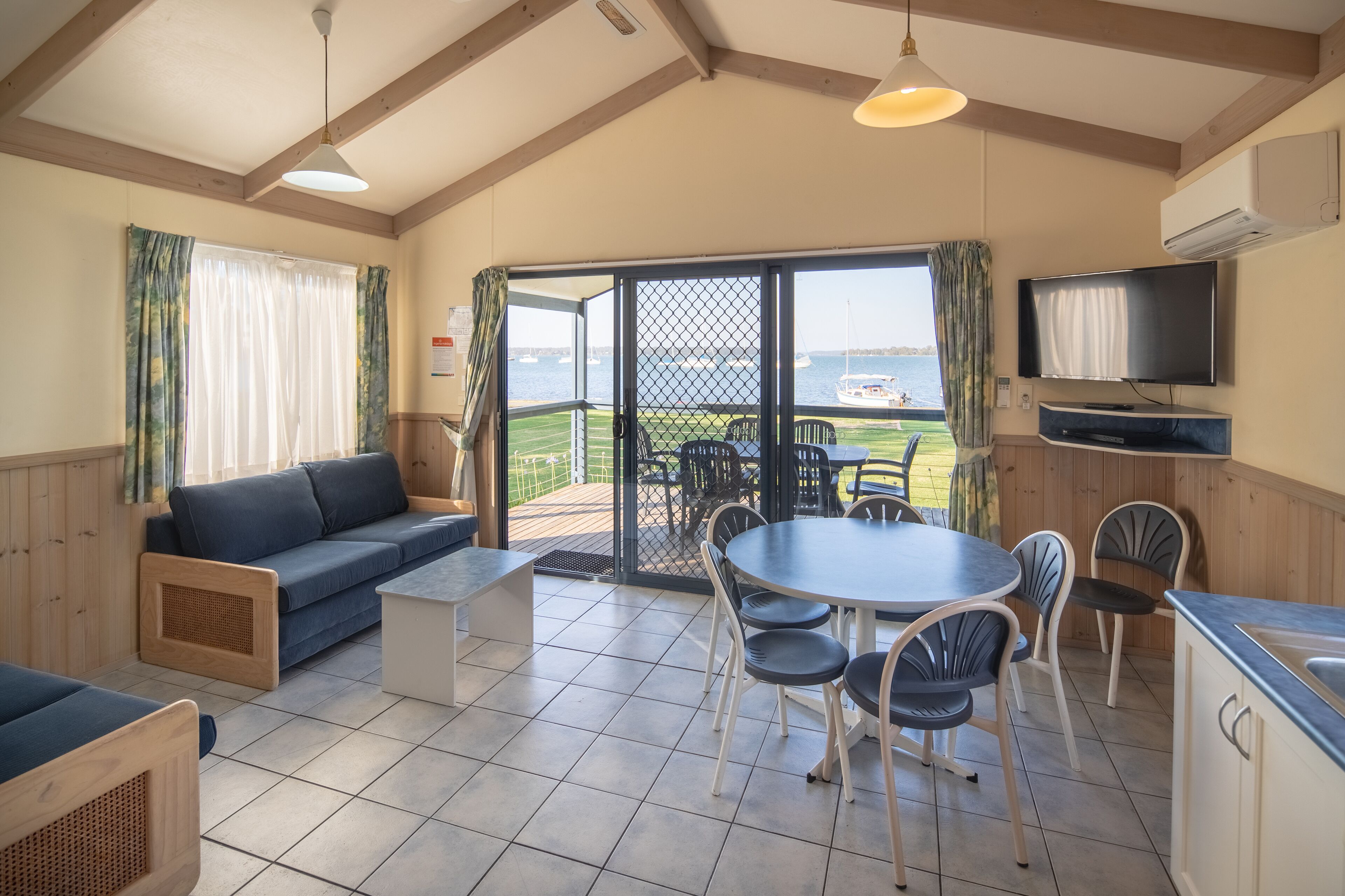 Une pièce confortable avec un canapé, une table à manger, des chaises et un téléviseur. Elle dispose d’une grande fenêtre offrant une vue sur la mer et les bateaux.