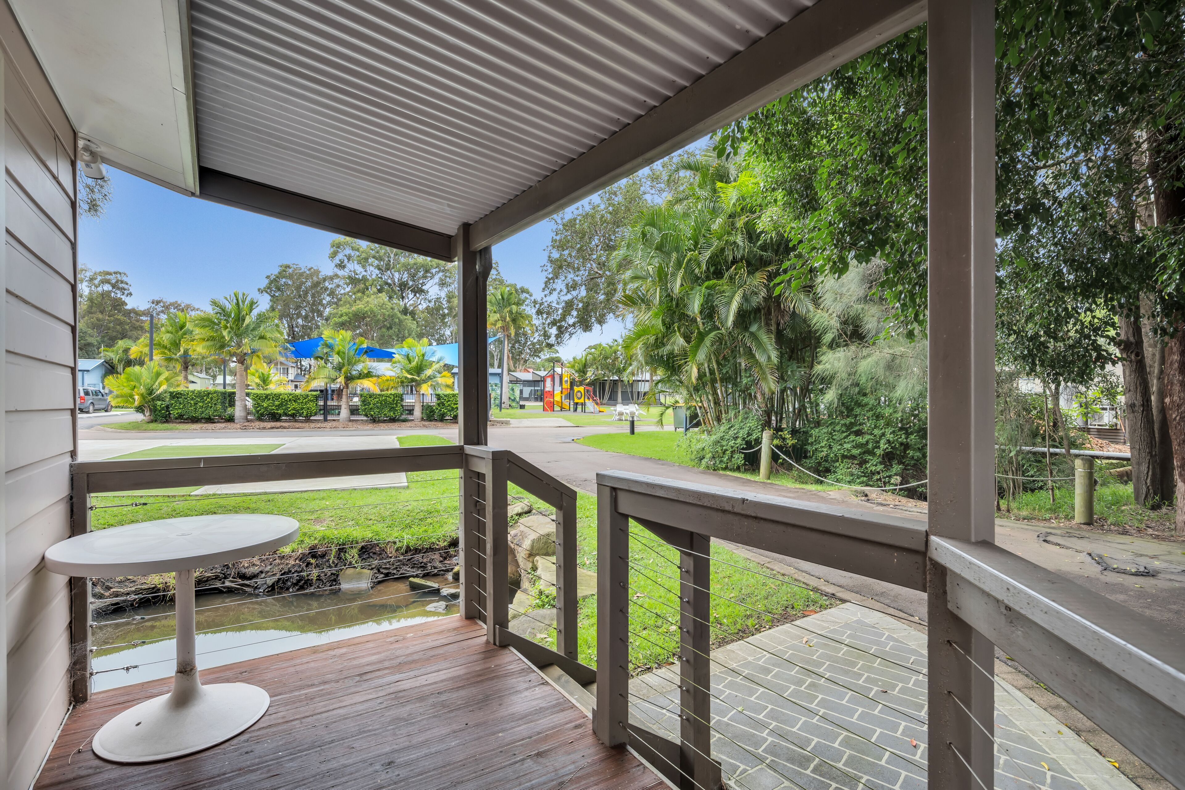 A covered outdoor area with a table and a view of a park with trees and playground equipment.